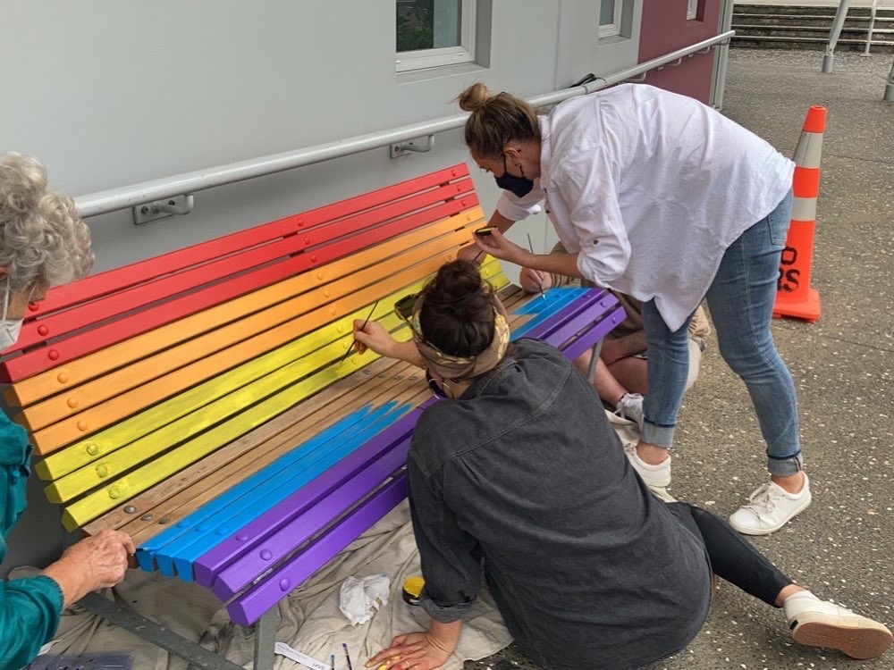 people painting a bench seat in rainbow colours
