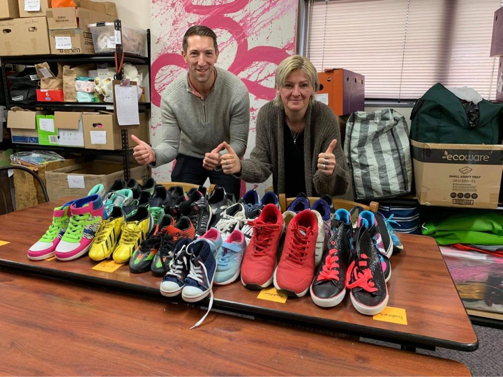 Two people with lots of donated sports shoes