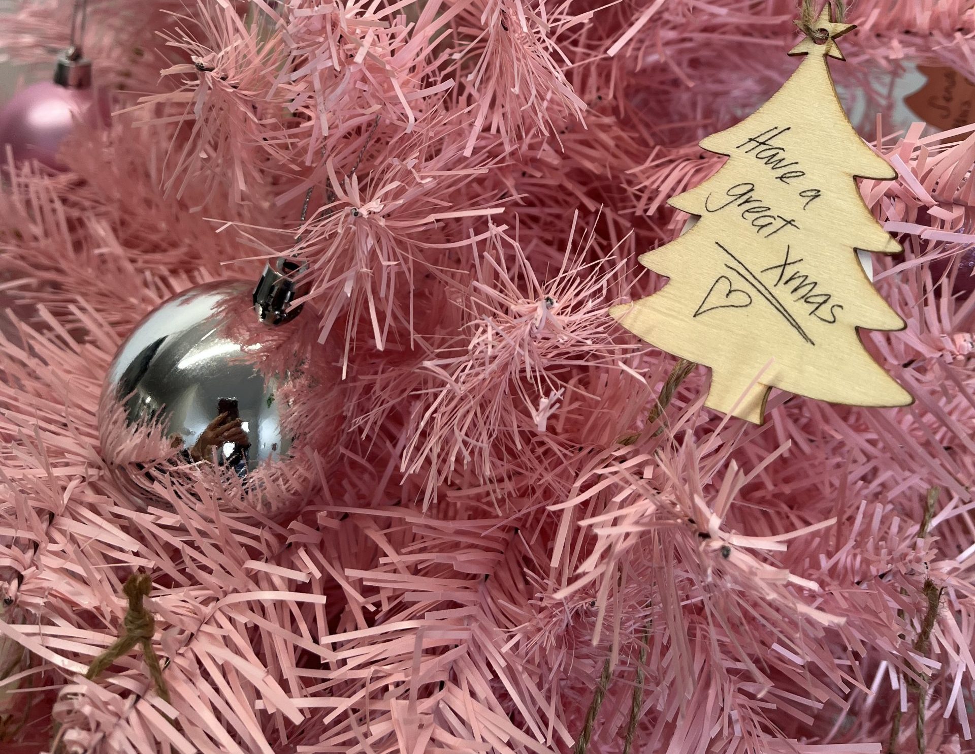 Close up of a soft pink tinsel christmas tree with silver and pink baubles and a tree shaped tag that has a handwritten note: "Have a great Xmas."