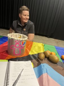 A person sits by a table draped in a rainbow flag